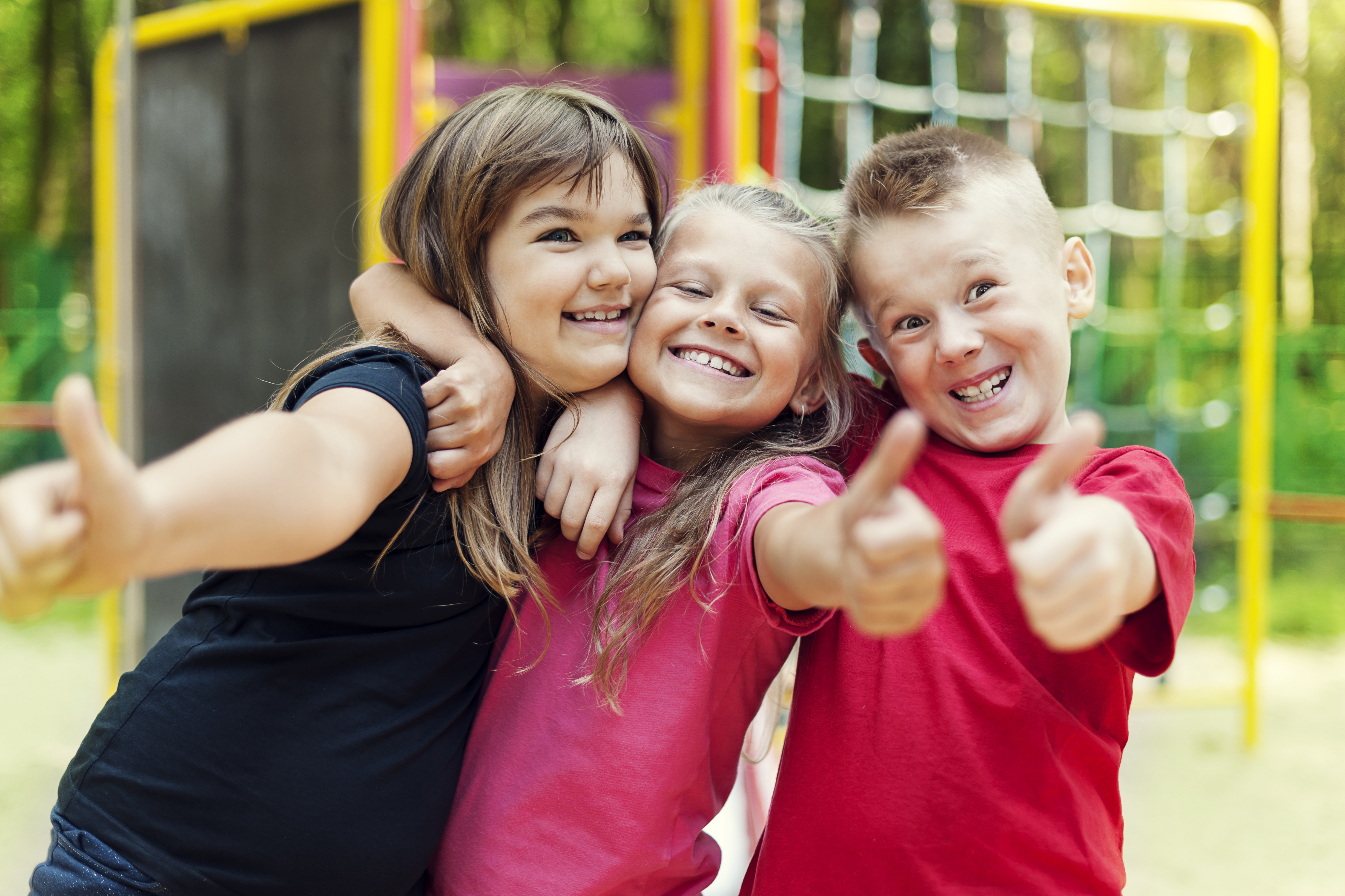 Middle school-age children smiling and showing thumbs up on a playground